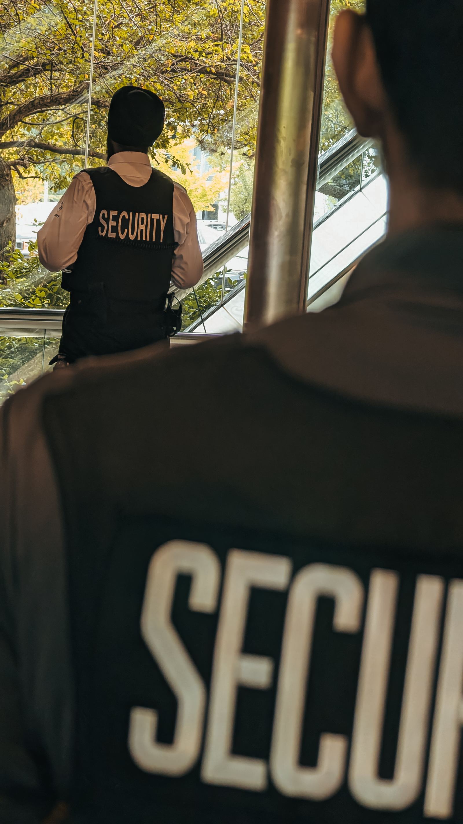 Two KingsGuard guards in marked security vests watching the entrance approach through a lobby window
