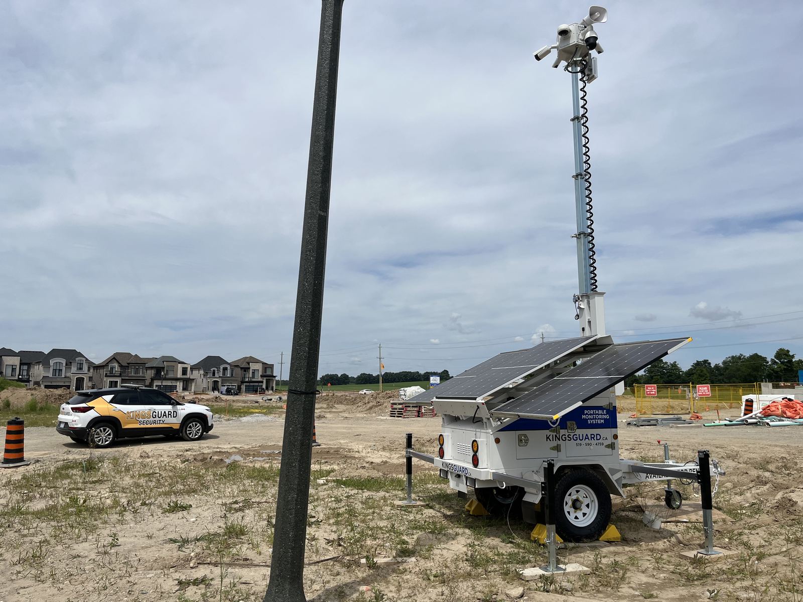 A KingsGuard solar-powered portable monitoring trailer with a raised camera mast on a residential construction site, with a branded KingsGuard SUV parked beside new homes
