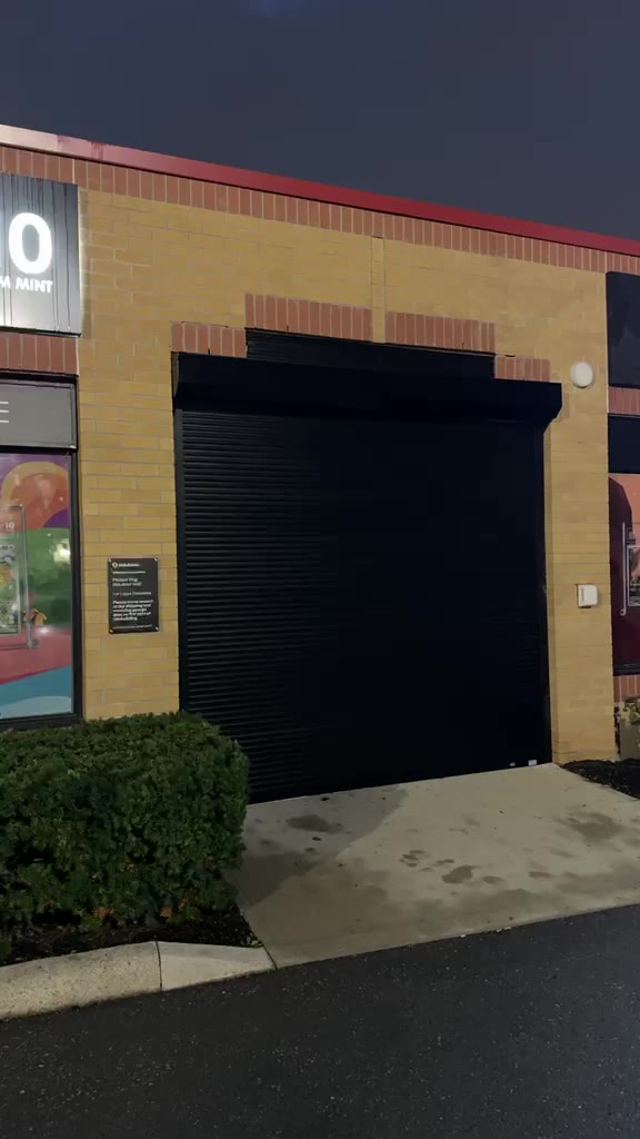 Motorized roll-down shutter closing and reopening over a retail storefront after hours.