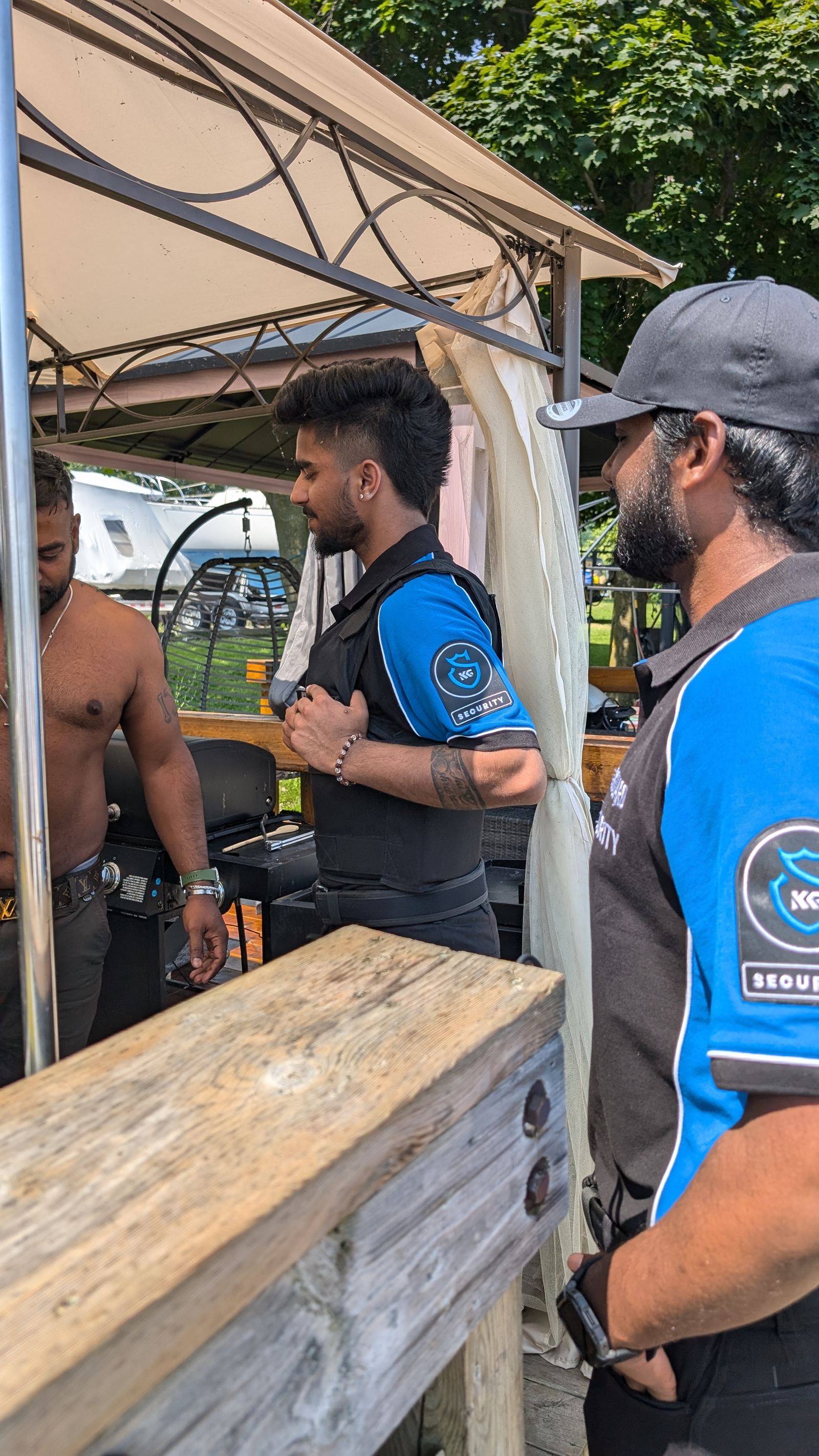 Three KingsGuard guards in branded shirts talking with staff under a canopy at an outdoor event